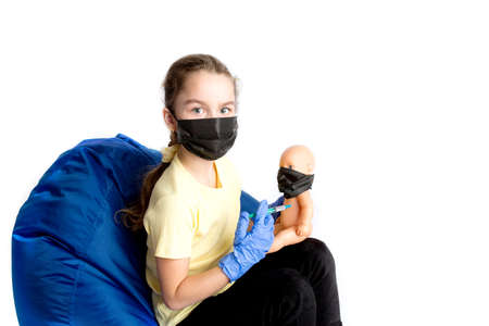 The girl plays a doctor with a doll. The reality of the coronavirus in the lives of children. Injection against covid19.の写真素材