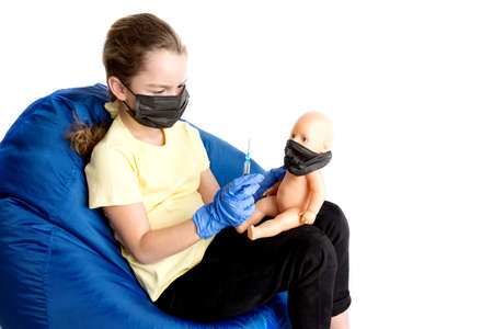 The girl plays a doctor with a doll. The reality of the coronavirus in the lives of children. Injection against covid19.の写真素材