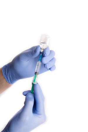 A doctors hand in a blue glove holding a syringe while taking liquid covid 19 corona virus vaccine. White background.の写真素材