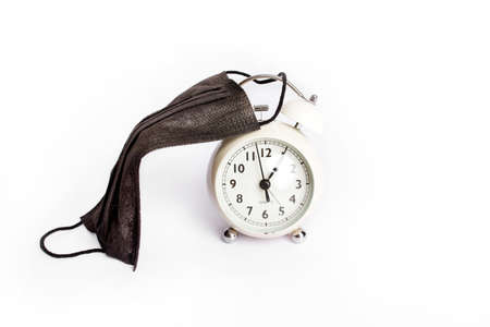 Vintage pink alarm clock with a face mask. Time until the end of quarantine, find a vaccine or new normal global conceptの写真素材