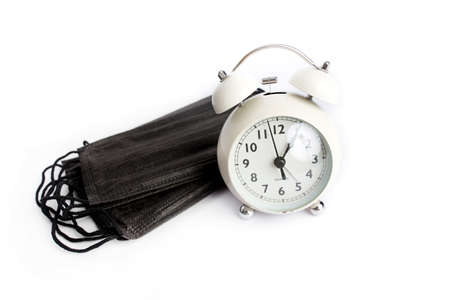 Vintage pink alarm clock with a face mask. Time until the end of quarantine, find a vaccine or new normal global conceptの写真素材