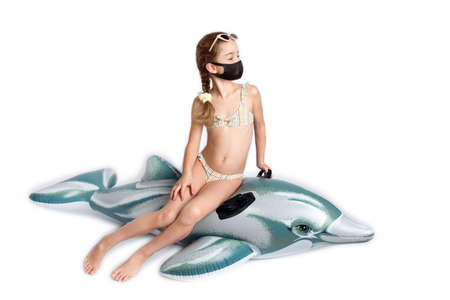 Child in a medical mask  in a bathing suit on an inflatable dolphin. Studio photography on a white background.の写真素材