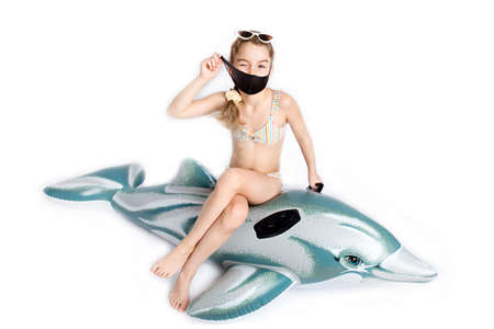 Child in a medical mask  in a bathing suit on an inflatable dolphin. Studio photography on a white background.の写真素材
