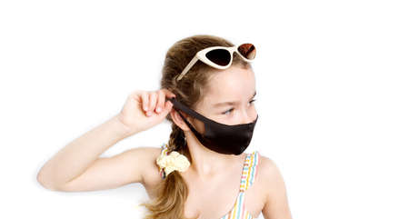 Happy little girl takes off protective medical black mask from face outdoors.の写真素材