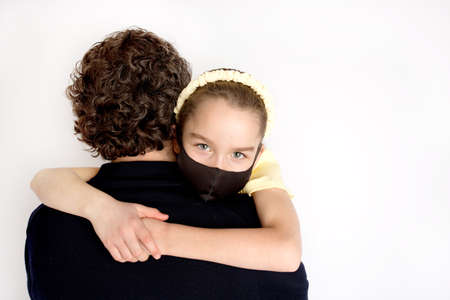 A girl in a black antibacterial mask and a yellow T-shirt in her fathers arms. The daughter hugs her father tightly.の写真素材