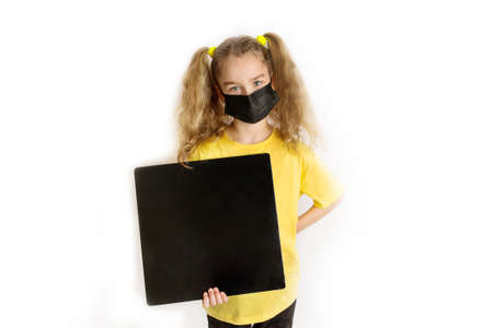 A girl in a black protective medical mask and a yellow T-shirt holds a black square for the inscription.の写真素材