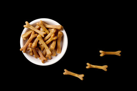 Close-up of brown dog food bones in a white dog bowl on a black studio background.の写真素材