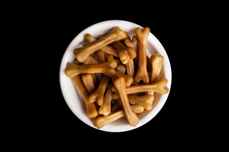Close-up of brown dog food bones in a white dog bowl on a black studio background.の写真素材