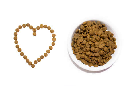 Dry food for cats and dogs in a white bowl. Heart from the food. Studio white background.の写真素材