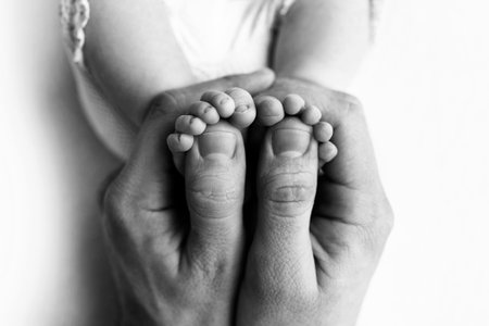 Feet of a newborn in the hands of a father, parent. Studio photography, black and white. Happy...
