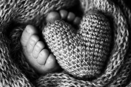 Feet of a newborn with a wooden heart, wrapped in a soft blanket. Black and white studio photography.の写真素材