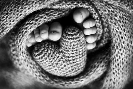 Feet of a newborn with a wooden heart, wrapped in a soft blanket. Black and white studio photography.の写真素材