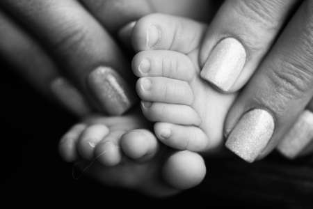Childrens feet in hold hands of mother and father on white. Mother, father and newborn Child. Happy Family people concept. Black and white.の写真素材