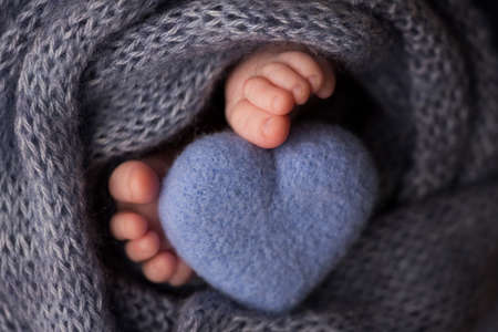 Two cute tiny baby feet wrapped in a blue-green aqua knitted blanket. And a knitted heart made of...
