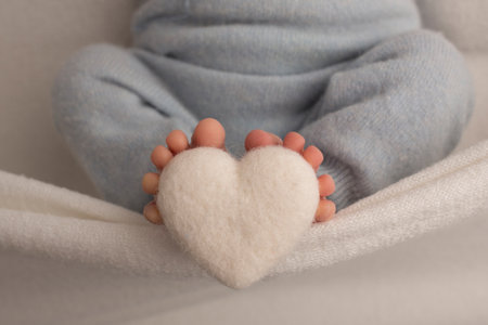 The feet of a newborn baby are wrapped in a knitted blanket. The fingers of a newborn baby are holding a white knitted heart.の写真素材