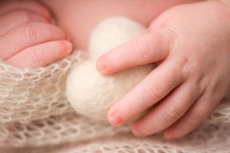 The hand and fingers of a newborn baby. The hand and fingers of a newborn baby. A baby holds a knitted white heart with his fingersの写真素材