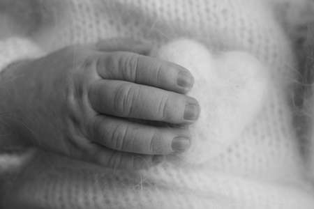 Tiny hand of a newborn baby. Soft hands of new born hold woolen heart. Fingers of a newborn baby...