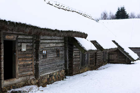 Winter Russian landscape. An old wooden hut, a log house with a thatched roof. Abandoned Russian village covered in snow. Log house with barn.の写真素材