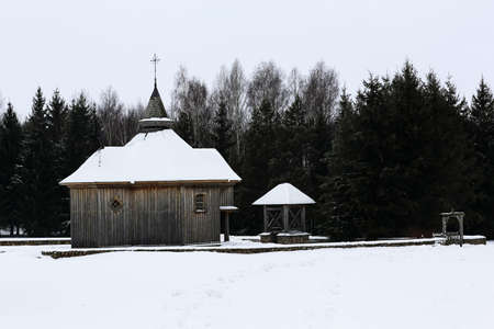 Old wooden church made of round logs. Cross on the dome. Winter Russian landscape. Snow covered trees. Abandoned old Russian village covered with snowの写真素材
