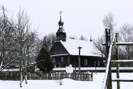 Old wooden church made of round logs. Cross on the dome. Winter Russian landscape. Snow covered trees. Abandoned old Russian village covered with snowの写真素材