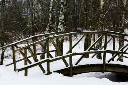 Old wooden bridge across the stream in the village. Winter Russian landscape. Snow covered trees. Abandoned Russian village covered in snow.の写真素材