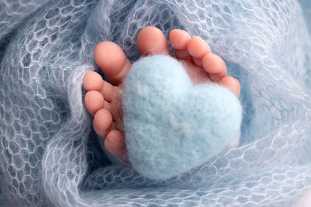 Knitted blue heart in the legs of a baby. Soft feet of a new born in a blue wool blanket. Close-up...