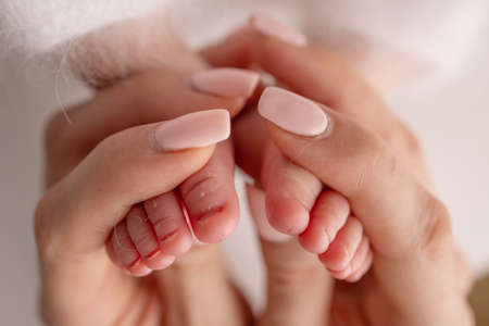 The palms of the parents. A father and mother hold the feet of a newborn child in a white blanket on...