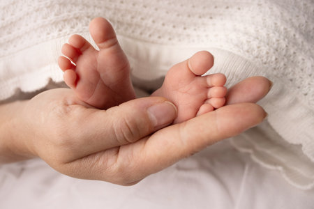 The palms of the parents. A mother hold the feet of a newborn child in a white blanket on a white...
