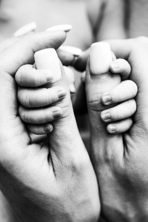 Hands of a sleeping newborn in the hands of the mother close-up. Tiny fingers of a newborn holding the thumbs of the mothers hand. Studio macro photography. Concepts of family and love. Black white.の写真素材
