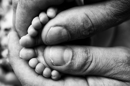 Mother is doing massage on her baby foot. Closeup baby feet in mother hands. Prevention of flat feet, development, muscle tone, dysplasia. Family, love, care, and health concepts. Black and white .の写真素材