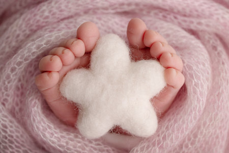 Knitted white star in the legs of a baby. Soft feet of a new born in a pink wool blanket. Close-up...