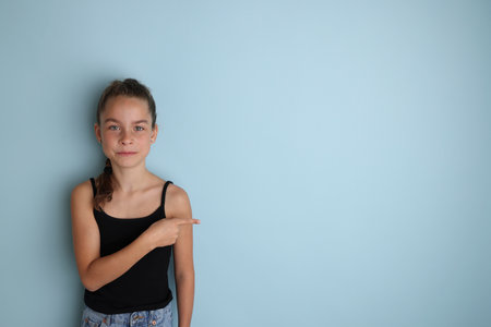 Little emotional teenage girl in a black t-shirt 11, 12 years old on an isolated blue background. Childrens studio portrait. Place the text to copy the place for the inscriptionの写真素材