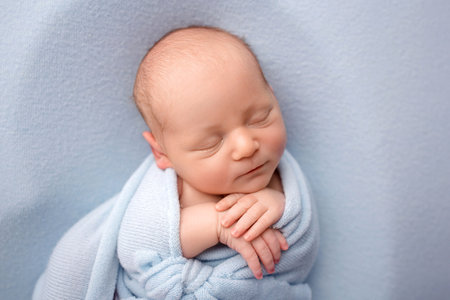 A cute newborn boy in the first days of life sleeps naked on a blue background.の写真素材