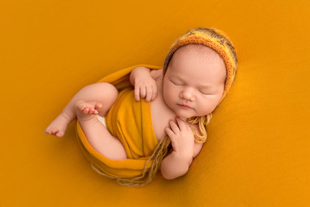 Top view of a newborn baby girl sleeping in an orange winding, in an orange bandage on her head, on an orange background. Beautiful portrait of a small newborn baby 7 days, one week old.の写真素材