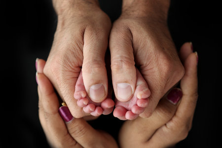 Feet of a newborn baby in the hands of parents. Happy Family oncept. Mum and Dad hug their babys legs. Studio photography on black background of a childs toes, heels and feet.の写真素材
