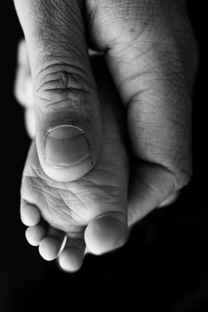 Mother is doing massage on her baby foot. Close up baby feet in mother hands on a black background. Prevention of flat feet, development, muscle tone, dysplasia. Black and white photo.の写真素材