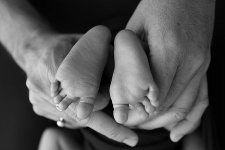 Black and white shade beautiful shape hands of mother, hold tiny newborn baby feet on black background with love, care, family safety and protection, child with premature birth concept or NICU careの写真素材