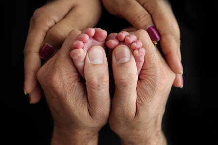 Feet of a newborn baby in the hands of parents. Happy Family oncept. Mum and Dad hug their babys legs. Studio photography on black background of a childs toes, heels and feet.の写真素材