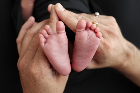 The palms of the parents. A mother hold the feet of a newborn child in a black blanket on a Black...