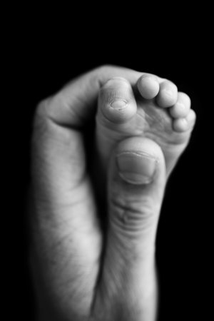 Close up baby feet in mother hands on a black background. Prevention of flat feet, development, muscle tone, dysplasia.Mother is doing massage on her baby foot.Black and white photo.の写真素材