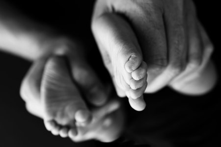 Black and white shade beautiful shape hands of mother, hold tiny newborn baby feet on black background with love, care, family safety and protection, child with premature birth concept or NICU careの写真素材