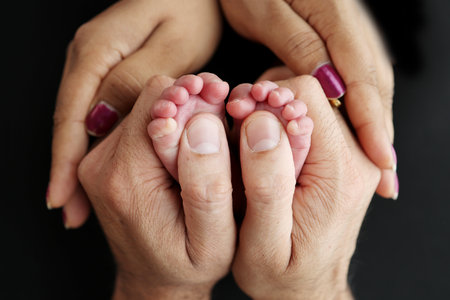 Feet of a newborn baby in the hands of parents. Happy Family oncept. Mum and Dad hug their babys legs. Studio photography on black background of a childs toes, heels and feet.の写真素材