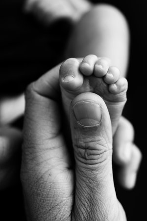 Close up baby feet in mother hands on a black background. Prevention of flat feet, development,...