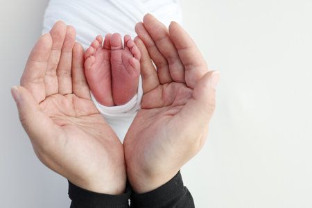 The palms of the father, the mother are holding the foot of the newborn baby in a white blanket. Feet of the newborn on the palms of the parents. Studio photography of a childs toes, heels and feet.の写真素材
