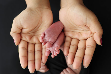 A mother hold the feet of a newborn child in a black blanket on Black backgroundの写真素材