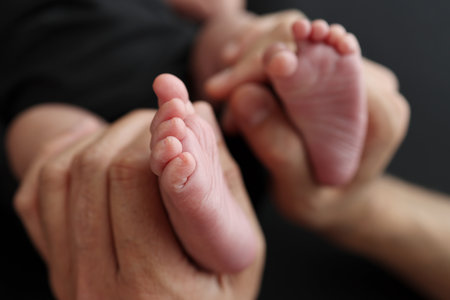 A mother hold the feet of a newborn child in a black blanket on a Black background. The feet of a newborn in the hands of parents. Studio macro photo legs, toes, feet and heels of a newborn.の写真素材