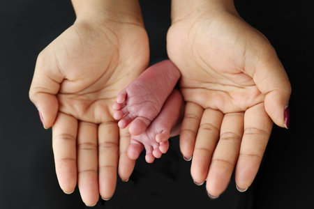 The palms of the parents. A mother hold the feet of a newborn child in a black blanket on a Black...