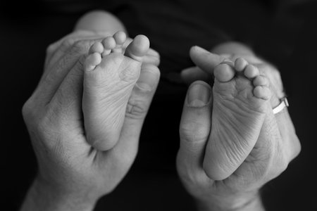 Black and white shade beautiful shape hands of mother, hold tiny newborn baby feet on black background with love, care, family safety and protection, child with premature birth concept or NICU careの写真素材