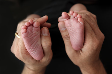 A mother hold the feet of a newborn child in a black blanket on a Black background. The feet of a...