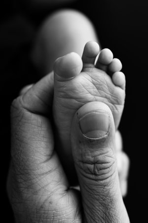 Close up baby feet in mother hands on a black background. Prevention of flat feet, development,...
